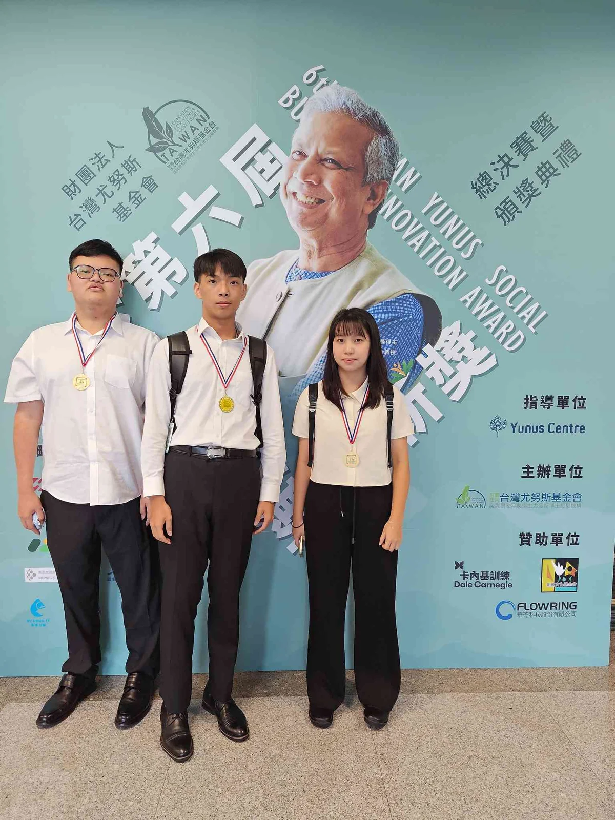 動域科技團隊三人在第六屆台灣尤努斯創新獎總決賽暨頒獎典禮背板前,配戴獎牌合影