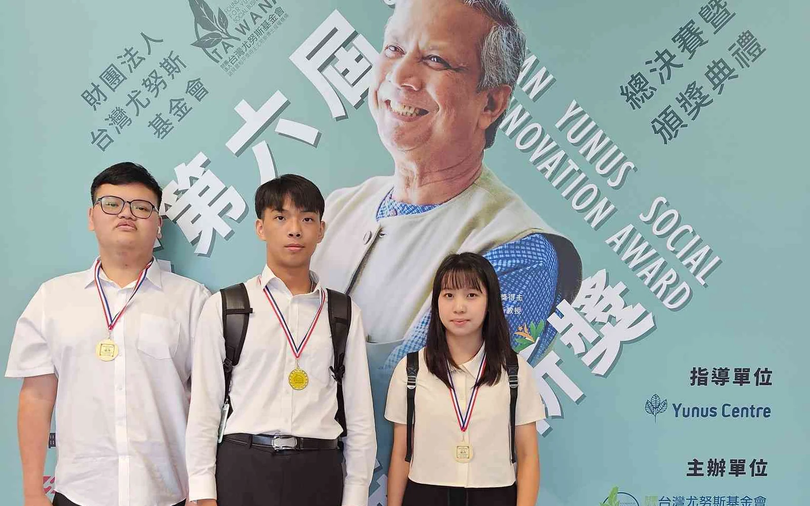 動域科技團隊三人在第六屆台灣尤努斯創新獎總決賽暨頒獎典禮背板前,配戴獎牌合影